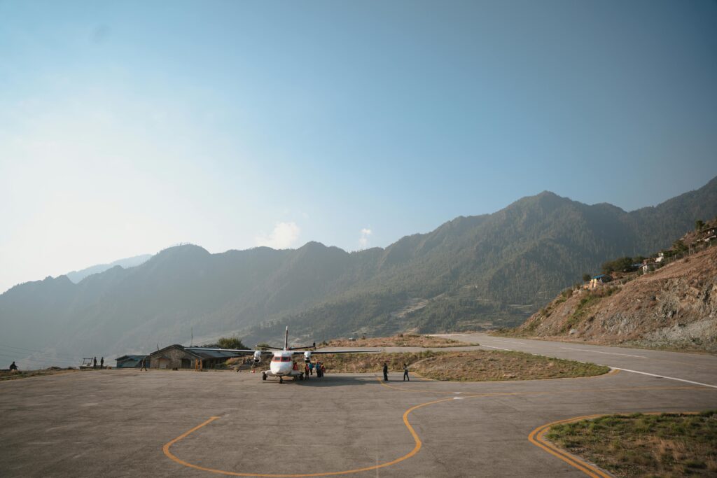A scenic view of a small aircraft on a mountain airstrip surrounded by lush green hills under a vibrant blue sky.