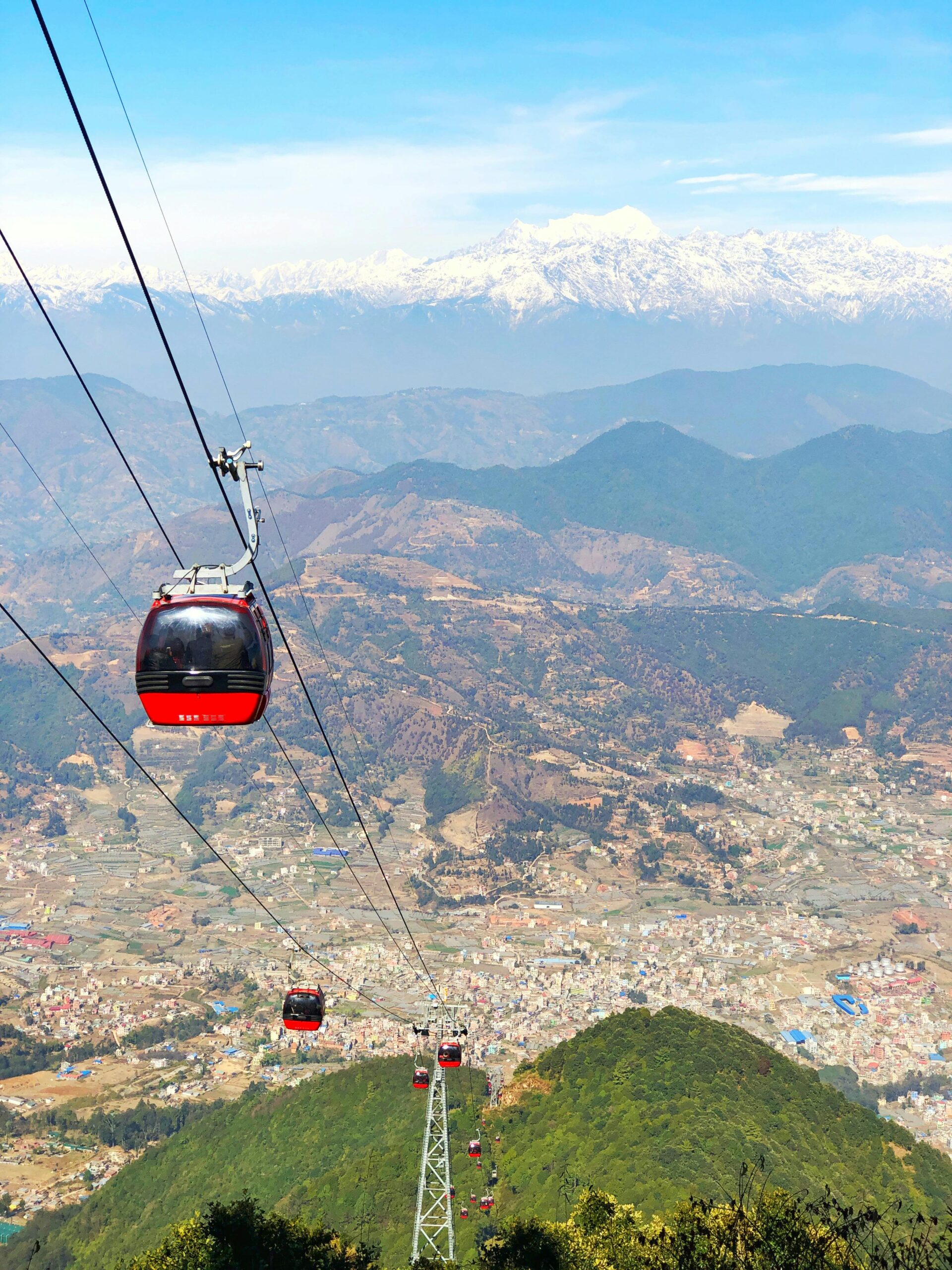 Breathtaking aerial view of cable cars over Chandragiri hills, Nepal with snow-capped mountains in the background.